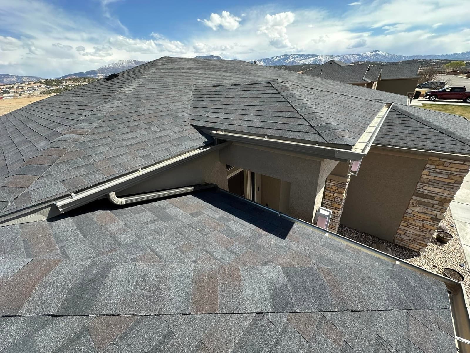 Close aerial of a new architectural shingle roof and fresh gutters with snow-capped Utah mountains beyond