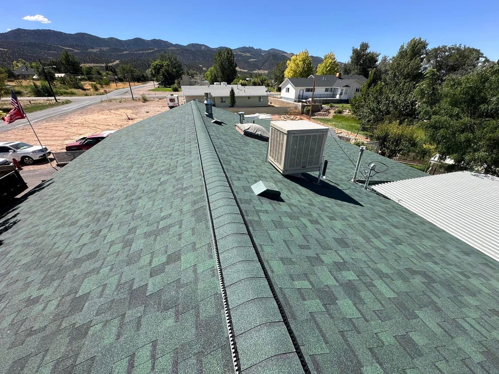 Freshly completed green shingle roof on a building in a Cedar City-area mountain town with pine trees and Utah peaks behind