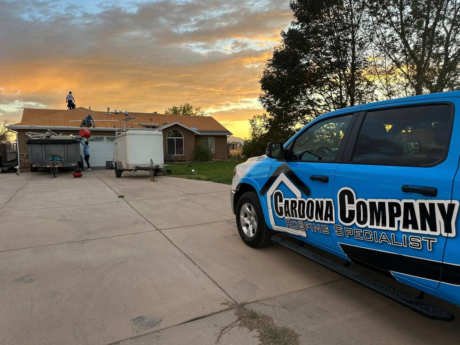 Cardona Company crew working a tear-off at golden hour with the branded blue truck in the driveway