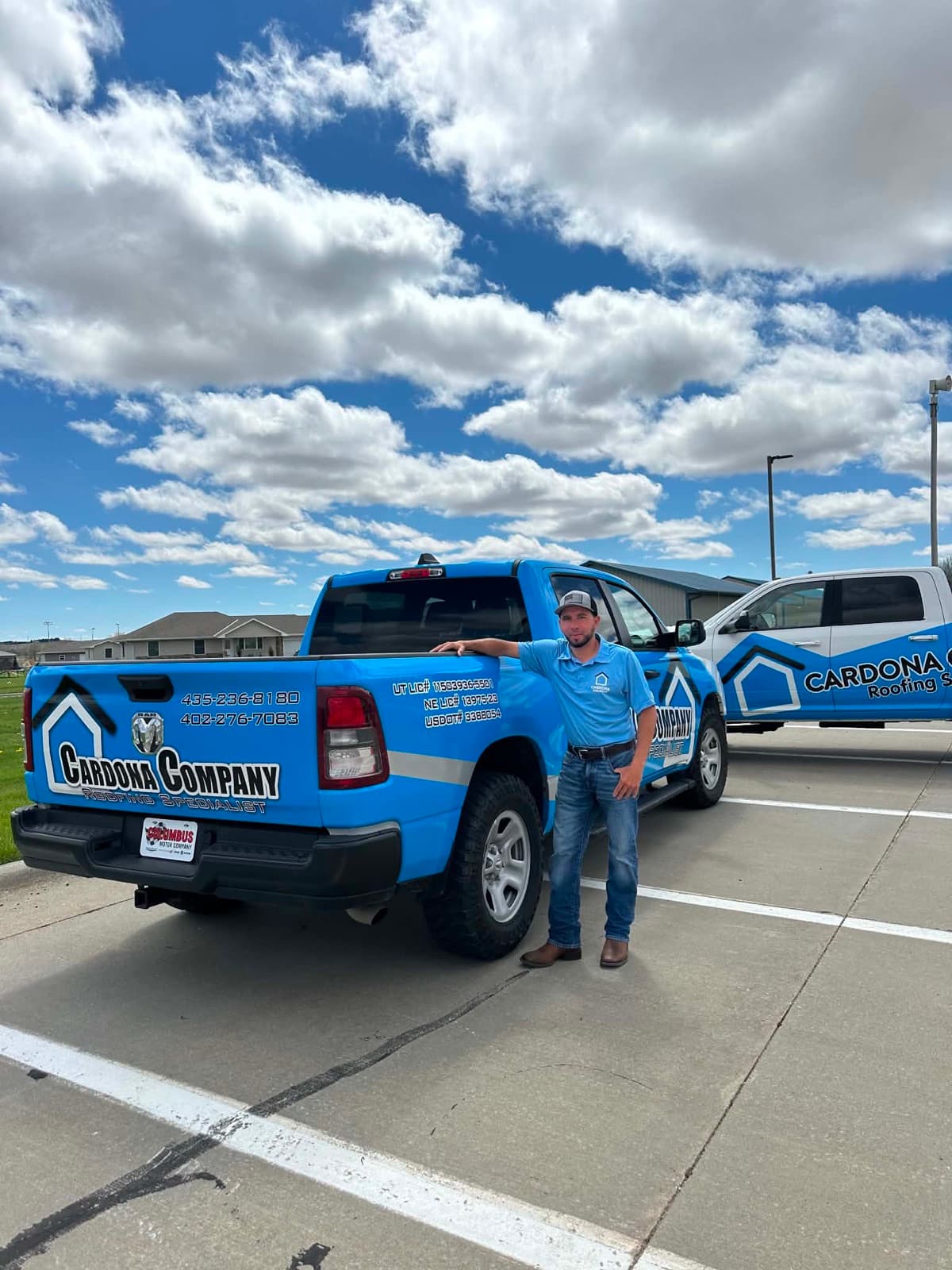 Gustavo Cardona standing with two branded Cardona Company Roofing Specialist trucks